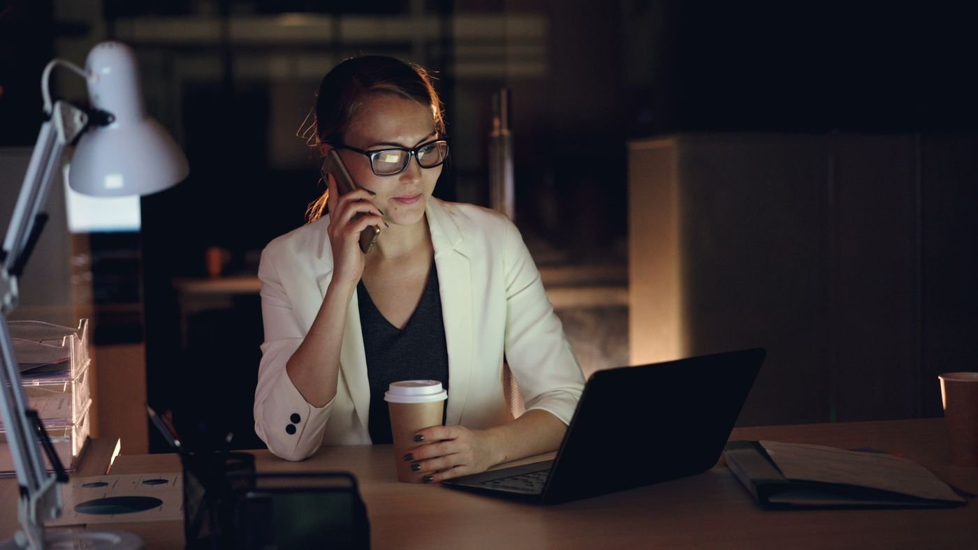 Unternehmerin arbeitet spätabends mit Kaffee am Laptop im Büro